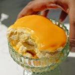 A hand holding a bowl with mango tiramisu.