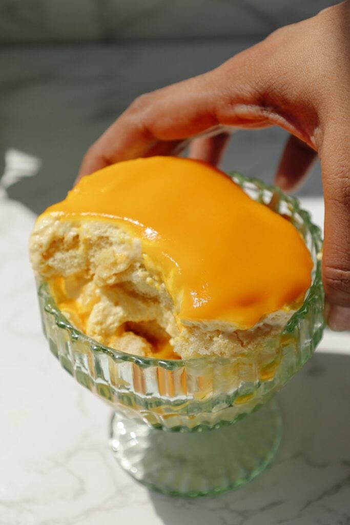A hand holding a bowl with mango tiramisu.