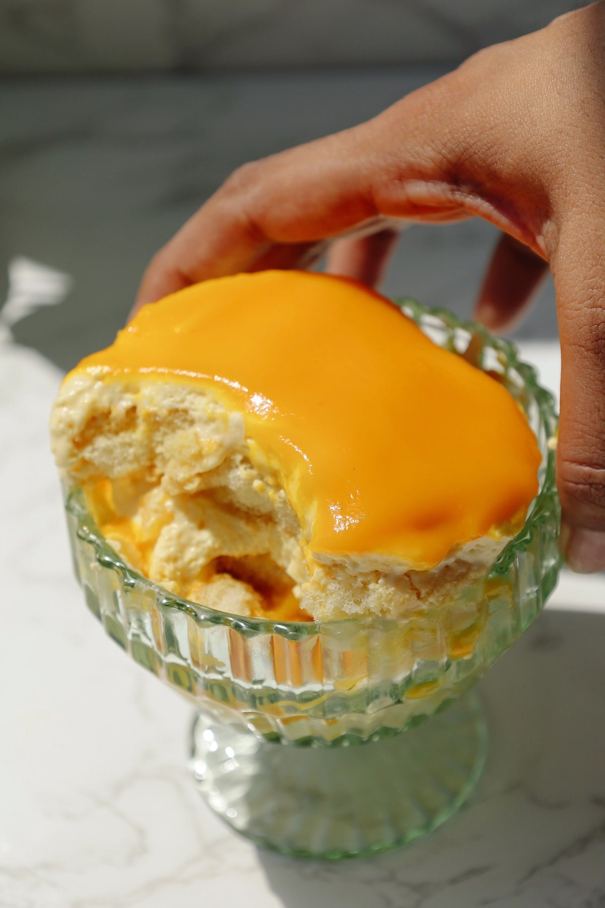 A hand holding a bowl with mango tiramisu.