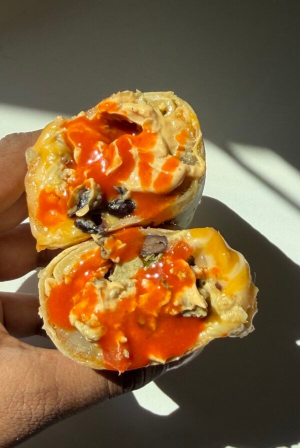 Hand holding a freezer breakfast burrito with hot sauce.