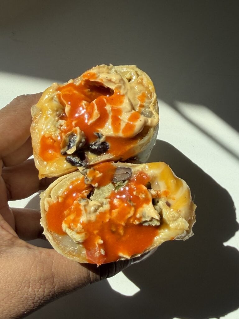 Hand holding a freezer breakfast burrito with hot sauce.