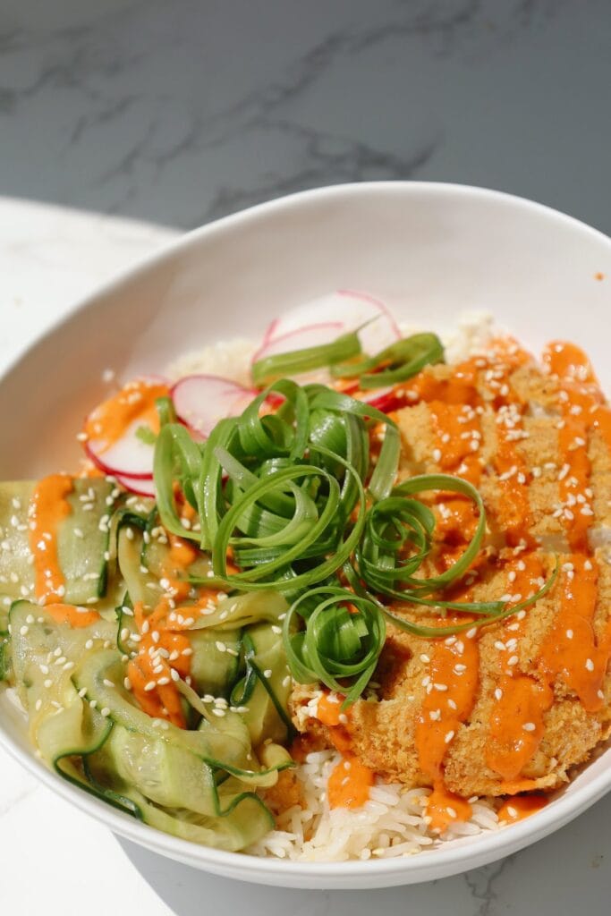 Tofu katsu bowl with sesame seeds and cucumbers.
