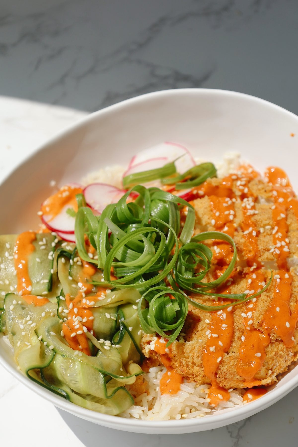Tofu katsu bowl with sesame seeds and cucumbers.