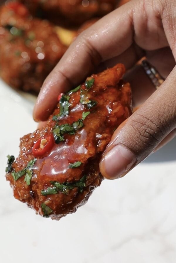 Thai sweet chili wing held in someone's hand.