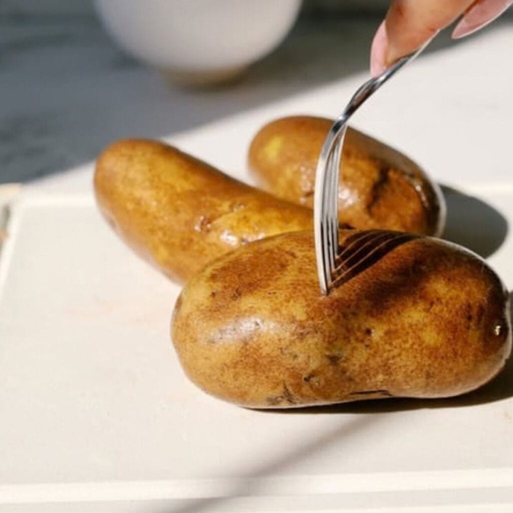a fork poking holes on the surface of raw potatoes, placed on a plate.