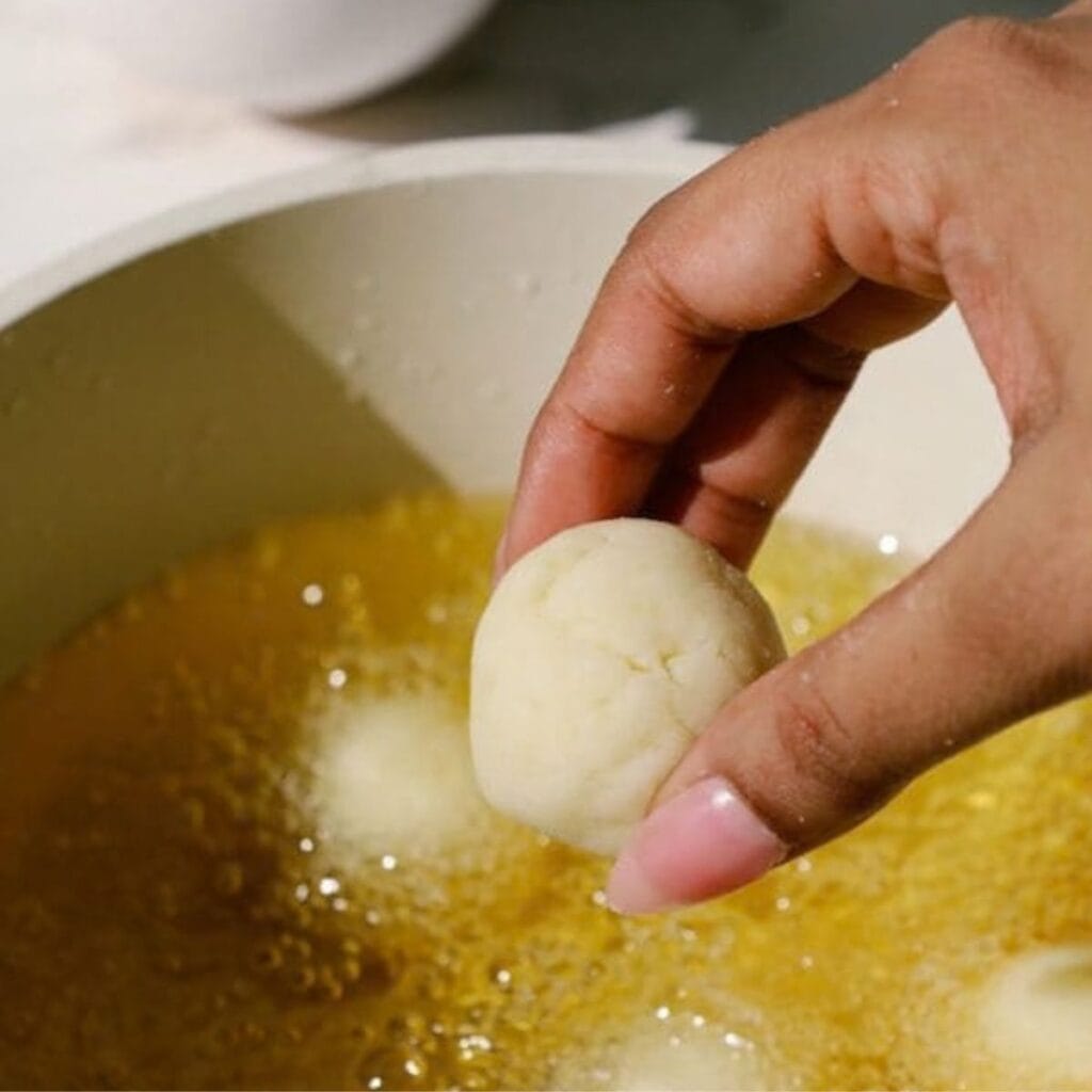 a hand dropping a mashed potato ball in a pan with hot oil.