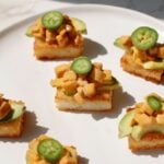 Six bites of crispy rice sushi displayed on a plate with avocado and jalapeno.