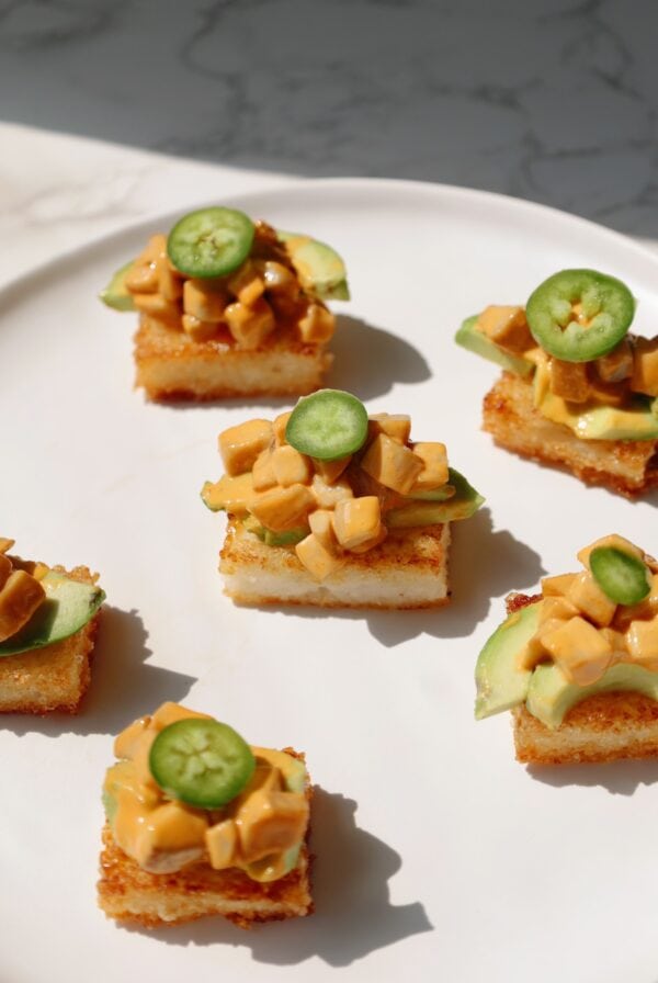 Six bites of crispy rice sushi displayed on a plate with avocado and jalapeno.