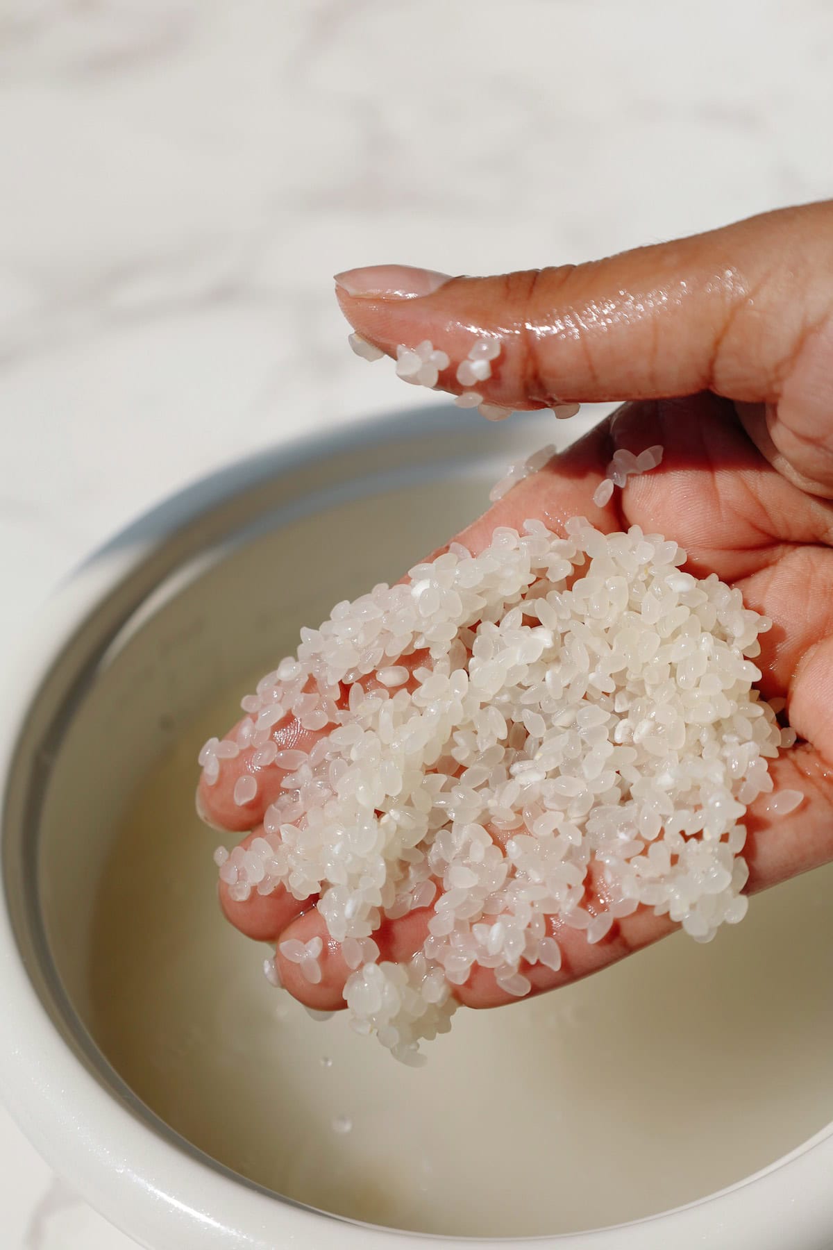 A hand washing rice in a pot.