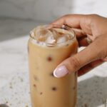 Chai latte in a tall clear glass with someone's hand around it.