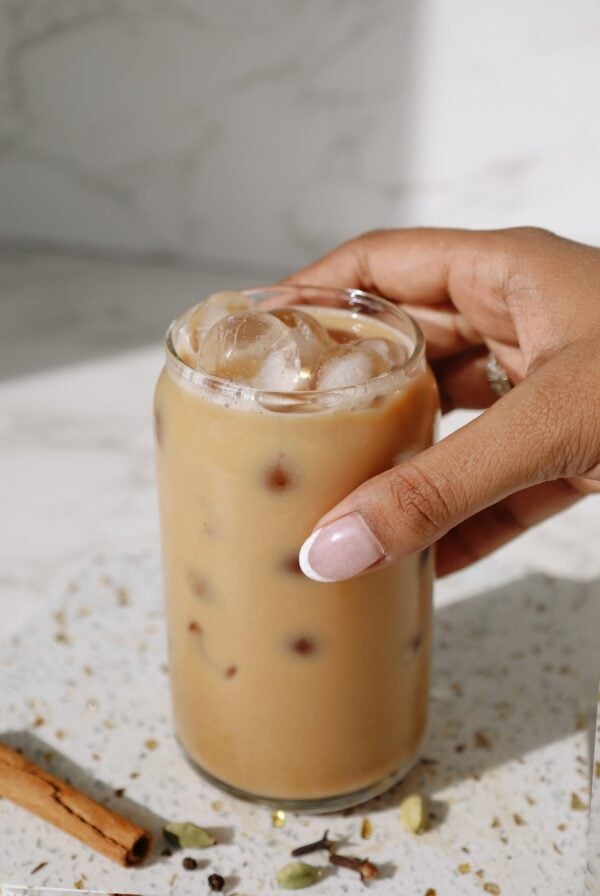 Chai latte in a tall clear glass with someone's hand around it.