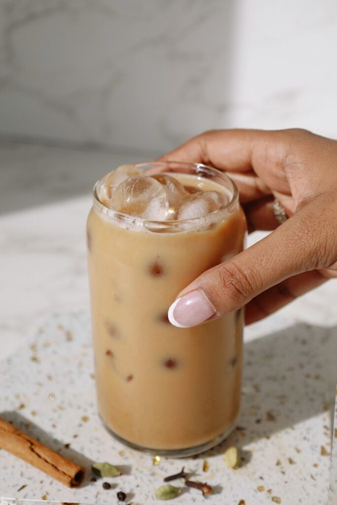Chai latte in a tall clear glass with someone's hand around it.