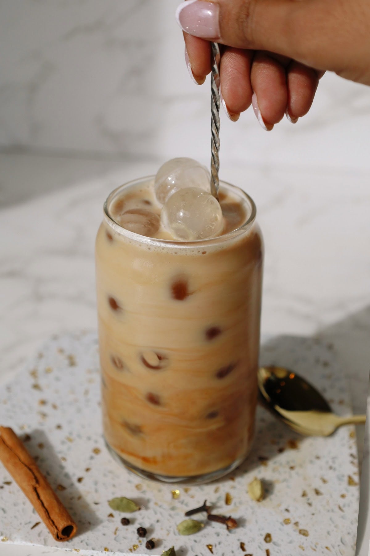 Stirring the milk in the iced chai with a long spoon.