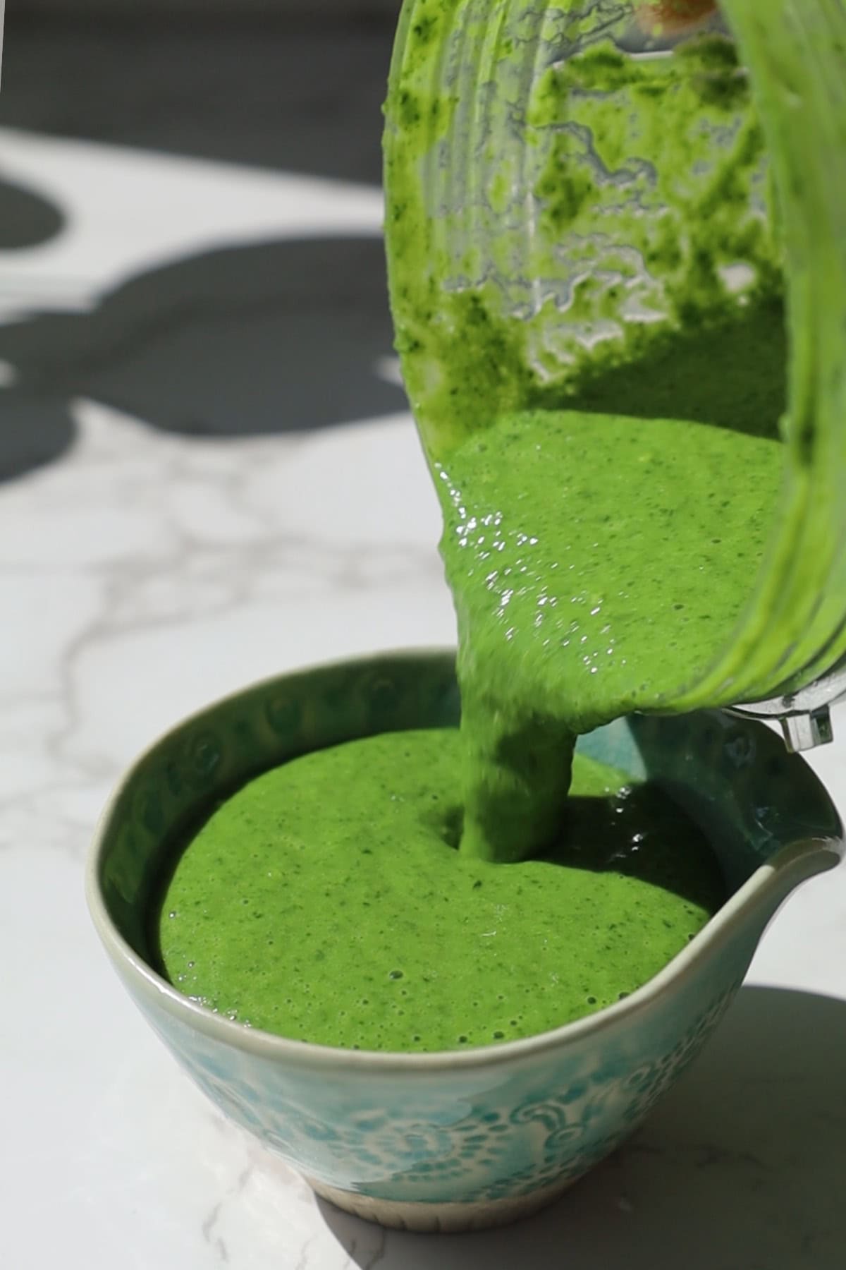 Blended creamy Indian mint chutney being poured into a bowl.