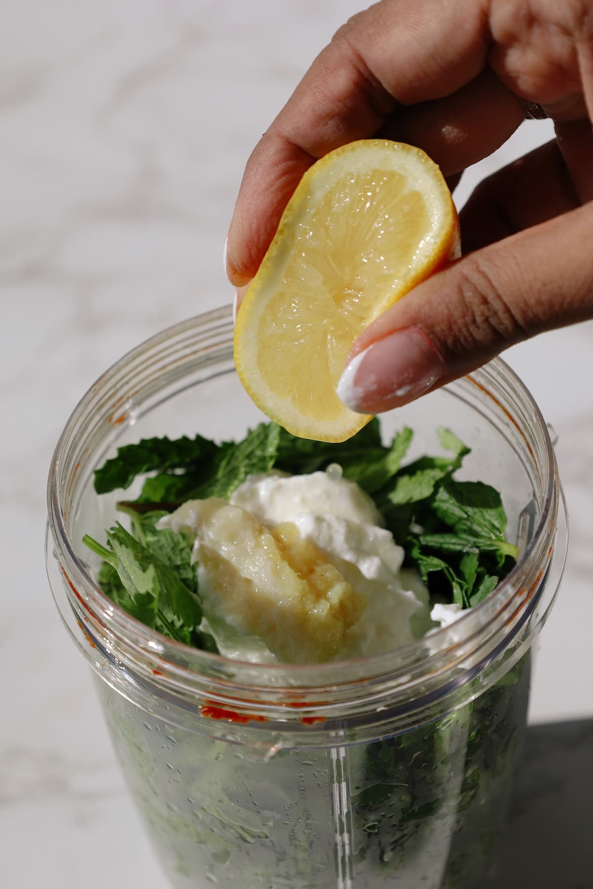 Fresh cilantro, mint, Greek yogurt, and aromatics in blender for homemade mint chutney.