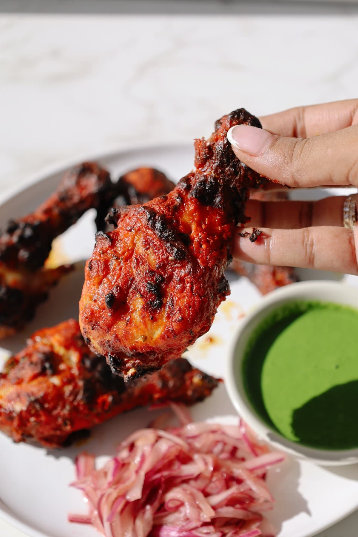 Close-up of hand holding smoky tandoori chicken drumstick with charred exterior.