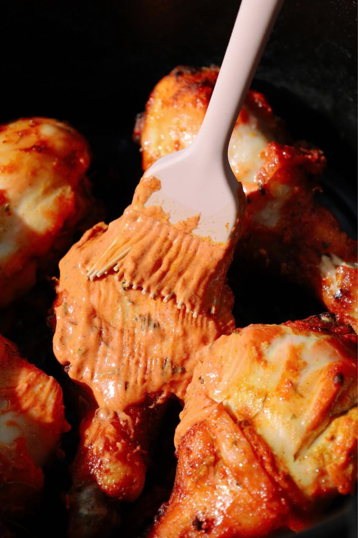 Brushing spiced yogurt marinade onto chicken drumsticks inside an air fryer basket.