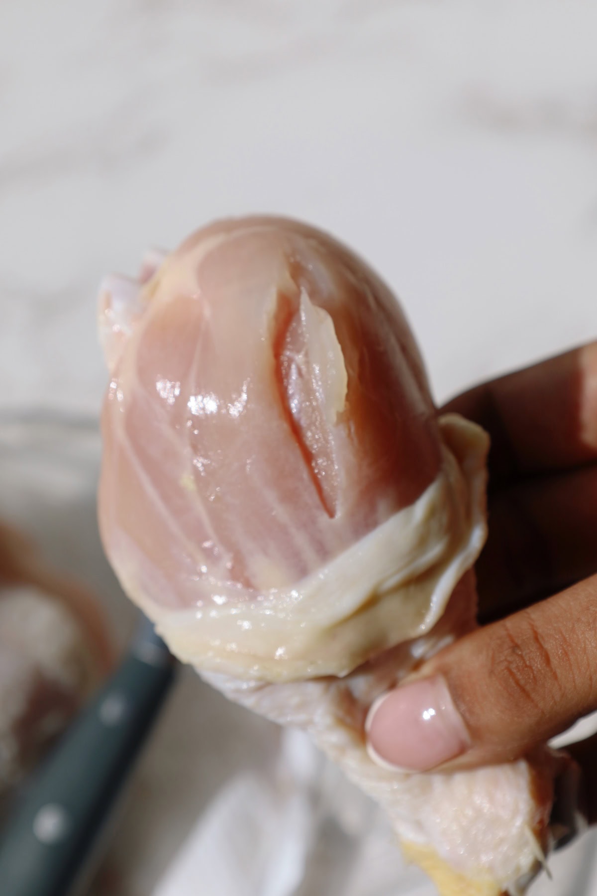 Close-up of raw chicken drumstick with shallow cuts.