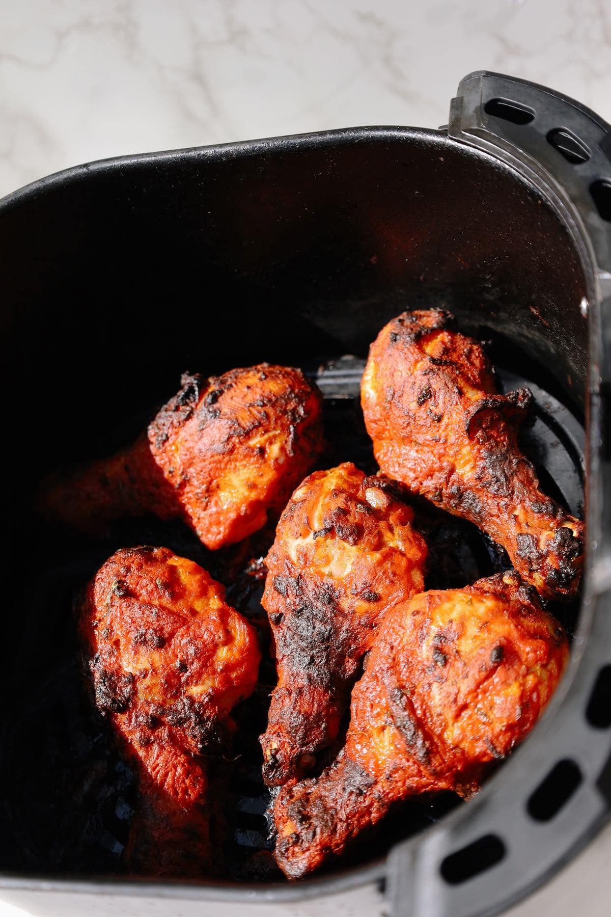 Fully cooked tandoori chicken drumsticks with charred edges inside air fryer.