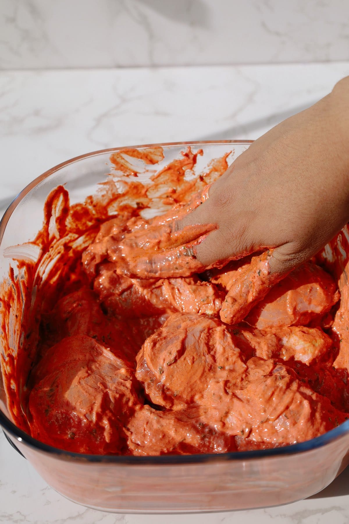 Coating raw chicken drumsticks with homemade tandoori yogurt and spice marinade.